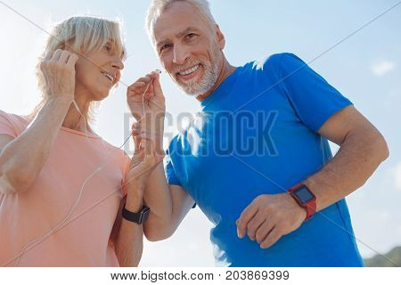 Sharing best things. Lovable elderly couple having a break in the morning run and listening to the music, sharing one pair of headphones