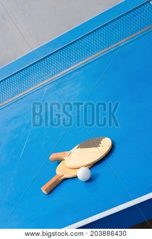 old pingpong rackets and ball and net on a blue pingpong table
