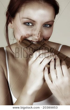 Mulher de cabelo vermelho bonito comer uma laje de chocolate com ele todo o seu rosto