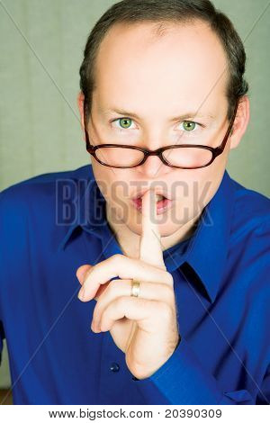Man met groene ogen in blauw shirt dragen van een bril veeleisende stilte met vinger naast zijn mond