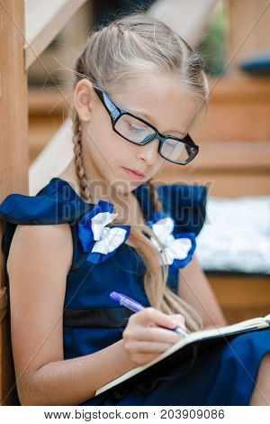 Adorable little school girl with notes and pencils outdoor.