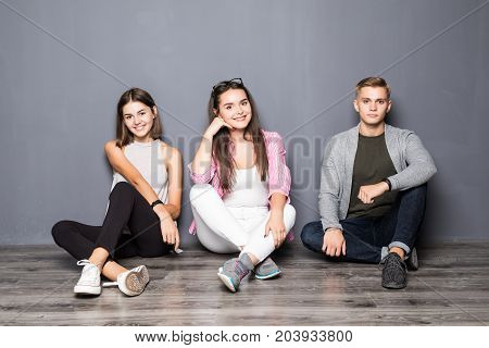 Group Of Friends Sitting On Floor On Gray Background