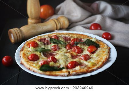 Hot pizza slice with melting cheese on a dark wooden table with tomatos.Gray drape.
