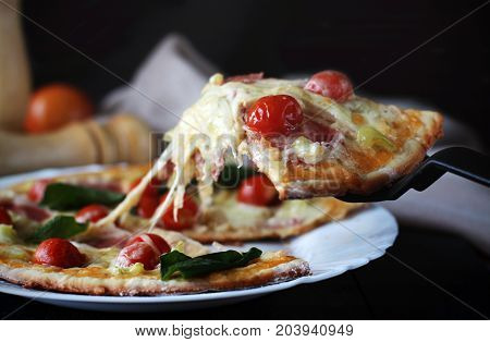 Hot pizza slice with melting cheese on a dark wooden table with tomatos.Gray drape.