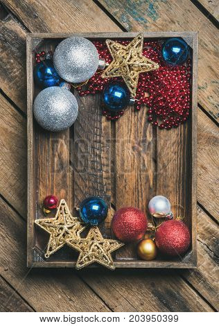 Flat-lay of Christmas or New Year holiday decoration background. Christmas tree glittering toy stars, balls and garland in wooden box over rustic wooden background, top view, copy space, verticalcomposition