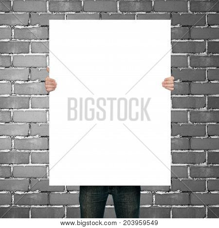man holding blank poster on gray brick background