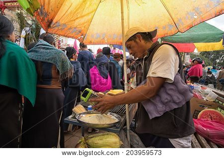 April 14 2017 CotacachiEcuador: man is grating cheese at a food stand on the edge of the indigenous kechwa crowd at the Easter procession