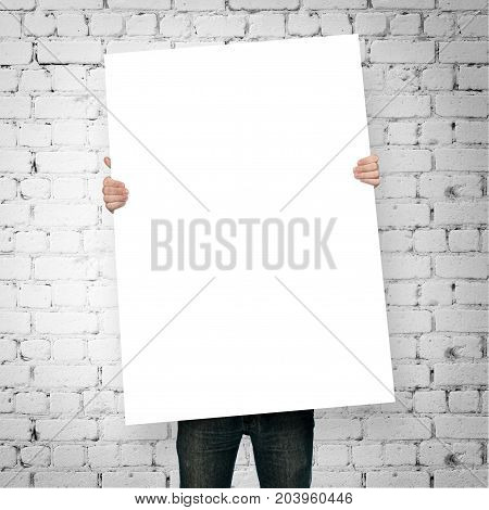 man holding blank poster on brick wall