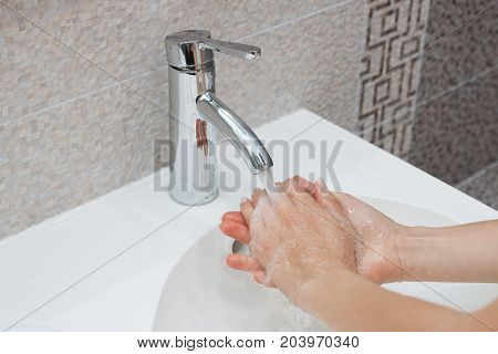 Washing of hands with soap under running water.