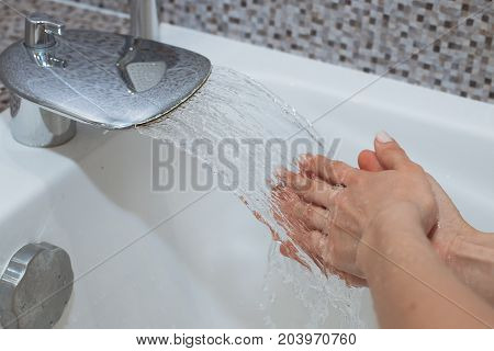 Washing of hands with soap under running water.