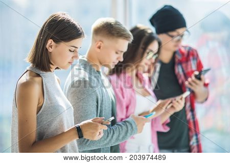 Group Of Young Friends Looking At Their Smart Phones Without Interacting Each Other Indoors. Concept