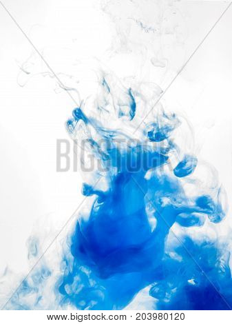Ink swirl in water isolated on white background. The blue paint in the water. Soft dissemination a droplets of blue ink in water close-up. Abstract vertical photo with soft focus, blurred backdrop.