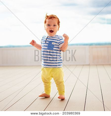 Portrait Of Cute Redhead, One Year Old Baby Boy Walking On Decking