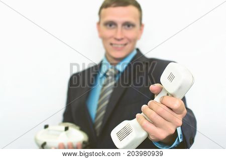 Contact us. Call us. Customer help service. Hot line consultant. Phone talk. Young smiling business man in suit holding phone handset in front of him.