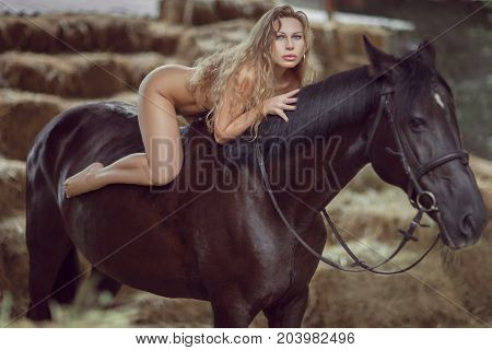Young naked woman is covered with long hair she is riding a horse.