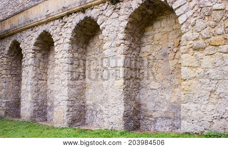 Arches in castle walls. There is a green lawn around the castle.