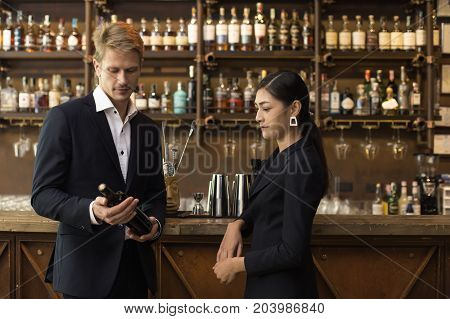 Man And Woman Looking To Bottle Wine At Bar, Man Present Wine To Woman For Dinner.