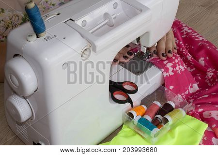 woman's hands using sewing machine with reels of colour threads. Workplace of tailor. people needlework and tailoring concept - tailor woman threading needle of sewing machine