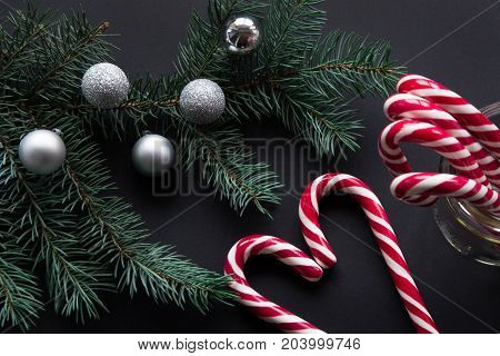 Christmas candy cane with silver evening balls and green fir tree on black background. Christmas concept. Top view and copy space close up.