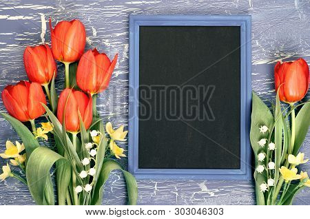 Blackboard And Bunch Of Red Tulips And Lily Of The Valley Flowers On Rustic Background. Space For Yo