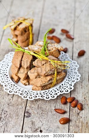 Fresh Italian cookies cantuccini stacked on white plate and almonds on ructic wooden table background. Sweet food.
