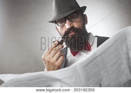 The Elegant Old-fashioned Bearded Man Is Smoking Pipe And Reading Newspaper.