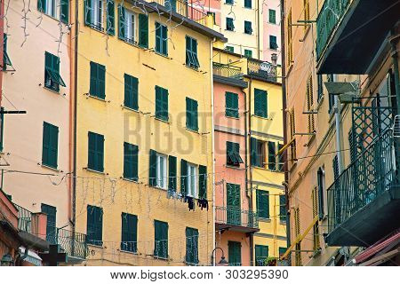 Facade Of Yellow And Pink Houses Of Riomaggiore With Green Windows With Wooden Shutters And Balconie