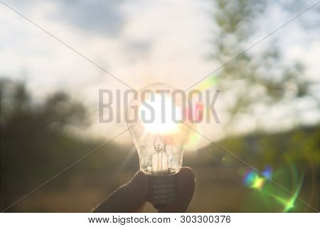 First Person View Of Person Hold Light Bulb Outside At The Nature, Enegry Concept With A Sunshine Th
