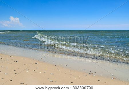Sea Waves Wash The Beach Against A Blue Sky. Landscape On A Wild Beach. The Sea In The Summer.