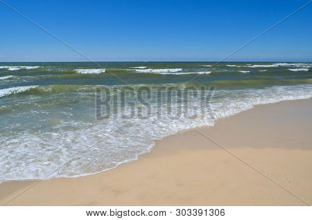 Sea Waves Wash The Beach Against A Blue Sky. Landscape On A Wild Beach. The Sea In The Summer.
