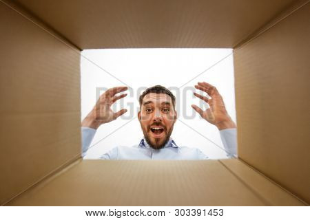 emotions, delivery and surprise concept - happy suprised man looking into open parcel box, from below