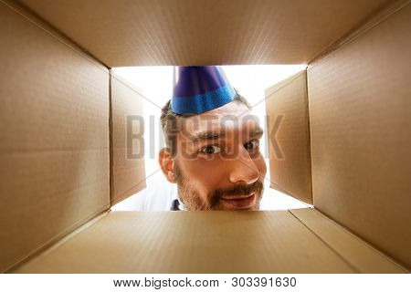 presents, delivery and surprise concept - happy man in party hat looking into open parcel box or birthday gift, from below