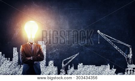Businessman With A Lightbulb In Place Of The Head Standing Next To A Blackboard Drawn With A City.  