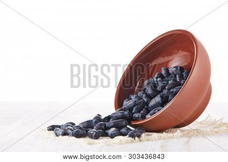 Honeysuckle berries in a ceramic bowl on a wooden table on white background.