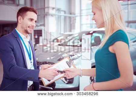 ?anager is giving a key to beautiful client of car dealership, both are smiling