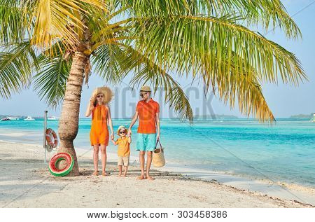 Family on beach, young couple in orange with three year old boy under the palm tree. Summer vacation at Maldives.