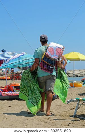 Street Vendor Walks On The Beach To Sell Its Colored Carpets To Tourists