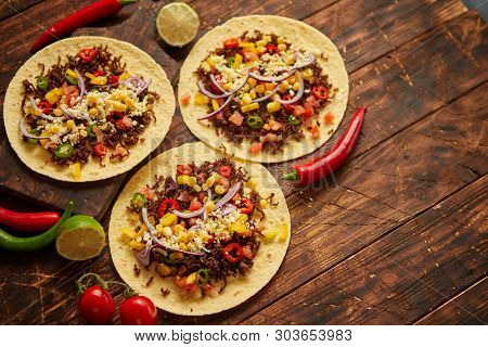 Healthy corn tortillas with grilled beef, fresh hot peppers, cheese, tomatoes over rusty wooden table background, top view, copy space. Mexican food contept.