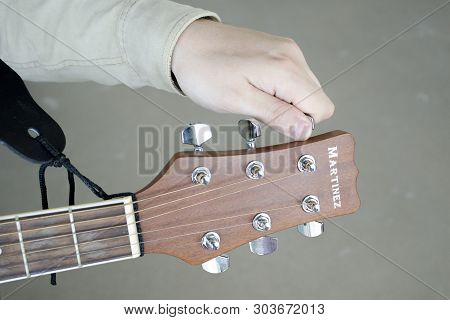 St. Petersburg, Russia - May 24, 2019: Man Tunes The Tuning Pegs On A Martinez Guitar On A Gray Back
