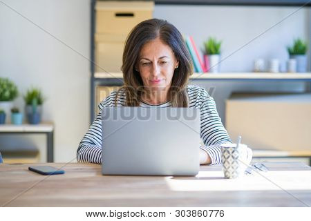 Middle age senior woman sitting at the table at home working using computer laptop Relaxed with serious expression on face. Simple and natural looking at the camera.