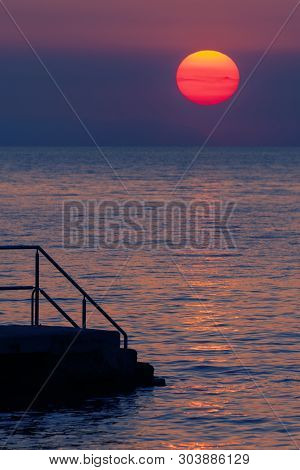 An Old Pier On Croatian Coast And Huge Orb Of Setting Sun In Background. Tourism, Travel And Vacatio