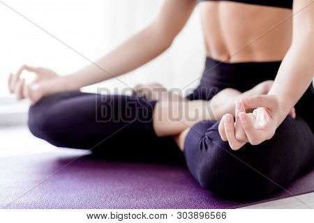 Closeup Of Slender Female Legs Folded Crossed In Lotus Pose. Young Athletic Girl In Black Uniform Is