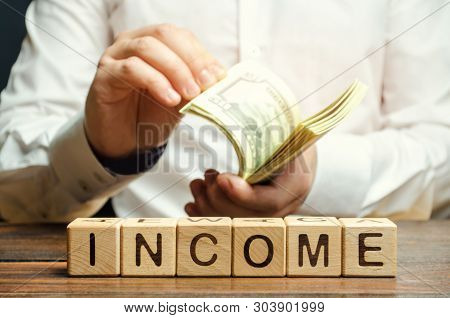 Wooden Blocks With The Word Income And Money In The Hands Of A Businessman. The Concept Of Revenue A