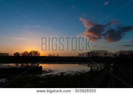 The Settting Sun Reflected In A Pool Of Water During Late Winter In East Flanders.