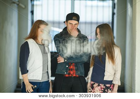 Vape Teenagers. Two Young Cute Girls In Casual Clothes Smoke Electronic Cigarettes Near Nonsmoking G