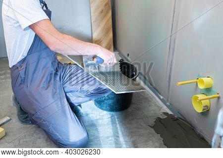 Ceramic Wood Effect Tiles. A Male Tiler Applies Mortar To The Back Of Ceramic Tiles To Install Porce