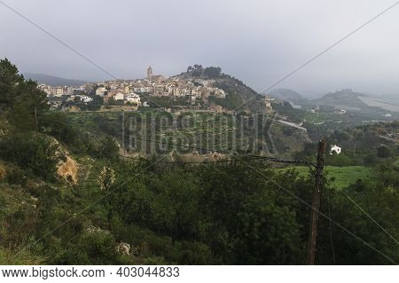 Panoramic view at a foggy morning in the hills of Polop de Marina with church and castell over green forest at the Costa Blanca, Spain