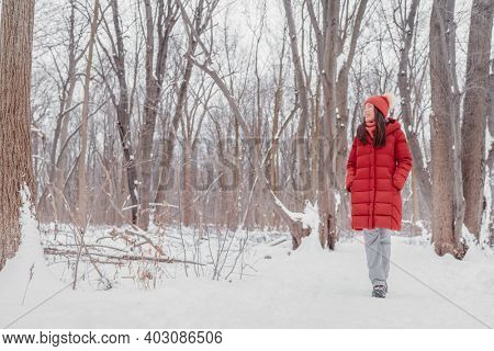 Happy Asian girl walking in snow path. Woman in red coat doing outdoor winter activity enjoying cold season.