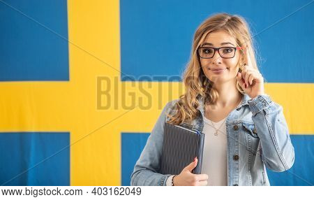 Warning Finger Up By Blonde Famel In Glasses Standing In Front Of Swedish Flag.
