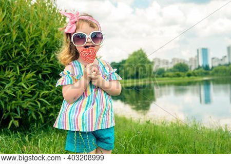 Fashionable Baby Girl, Sunglasses, Lollipop Like A Heart.little Three Year Old Girl Licks A Colored 